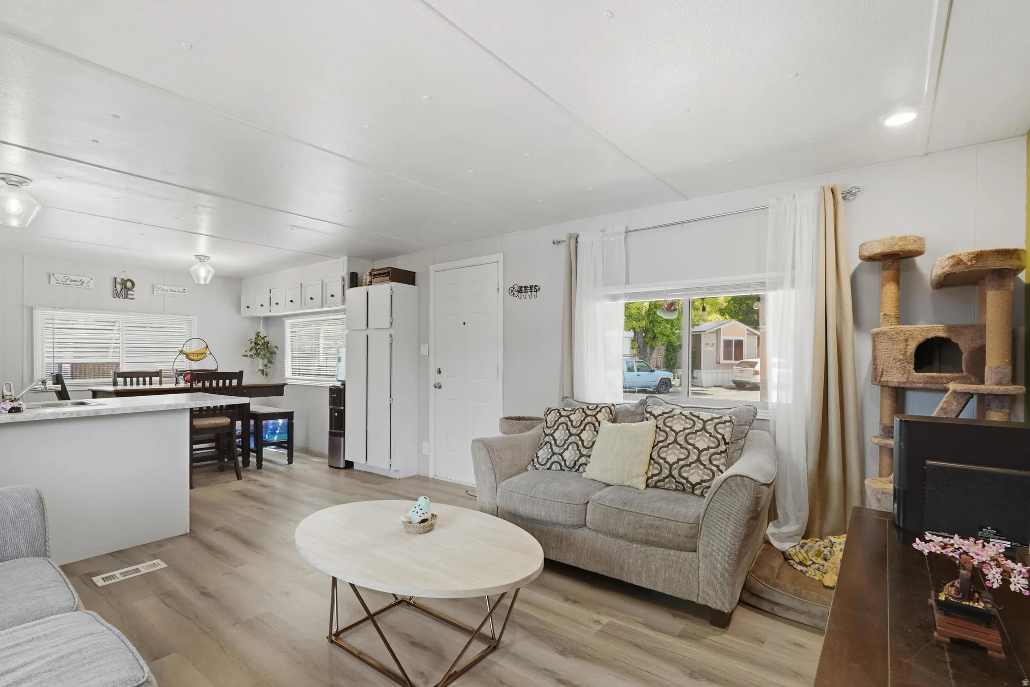 Open-concept living space featuring wood-finish flooring, recessed lighting, and a white kitchen with upper cabinetry and a built-in refrigerator