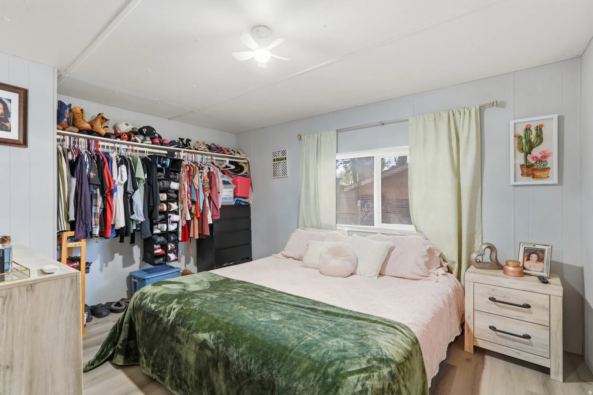 Bedroom featuring wood-finish flooring, a ceiling fan, and light blue wall panels