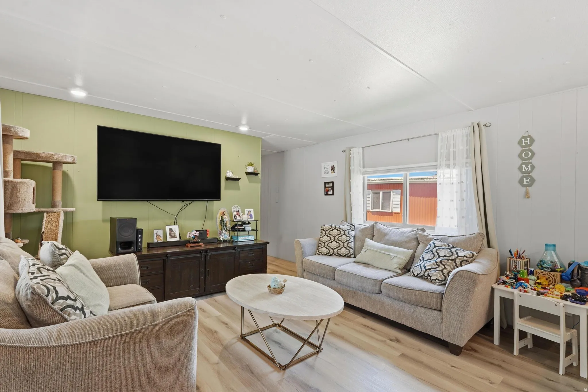 Spacious living area featuring light wood-finish flooring, recessed lighting, and a window with sheer curtains