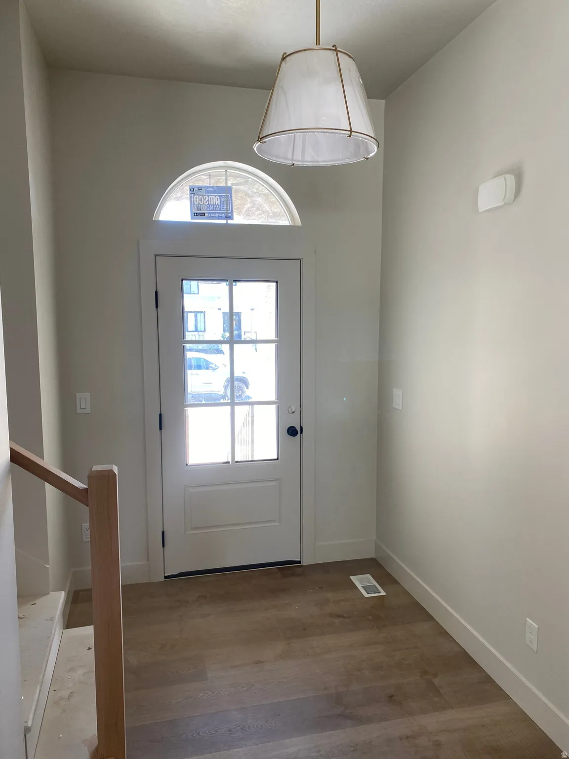 Entryway featuring a glass-paneled door with an arched transom window, wood-finish flooring, and a contemporary pendant light fixture