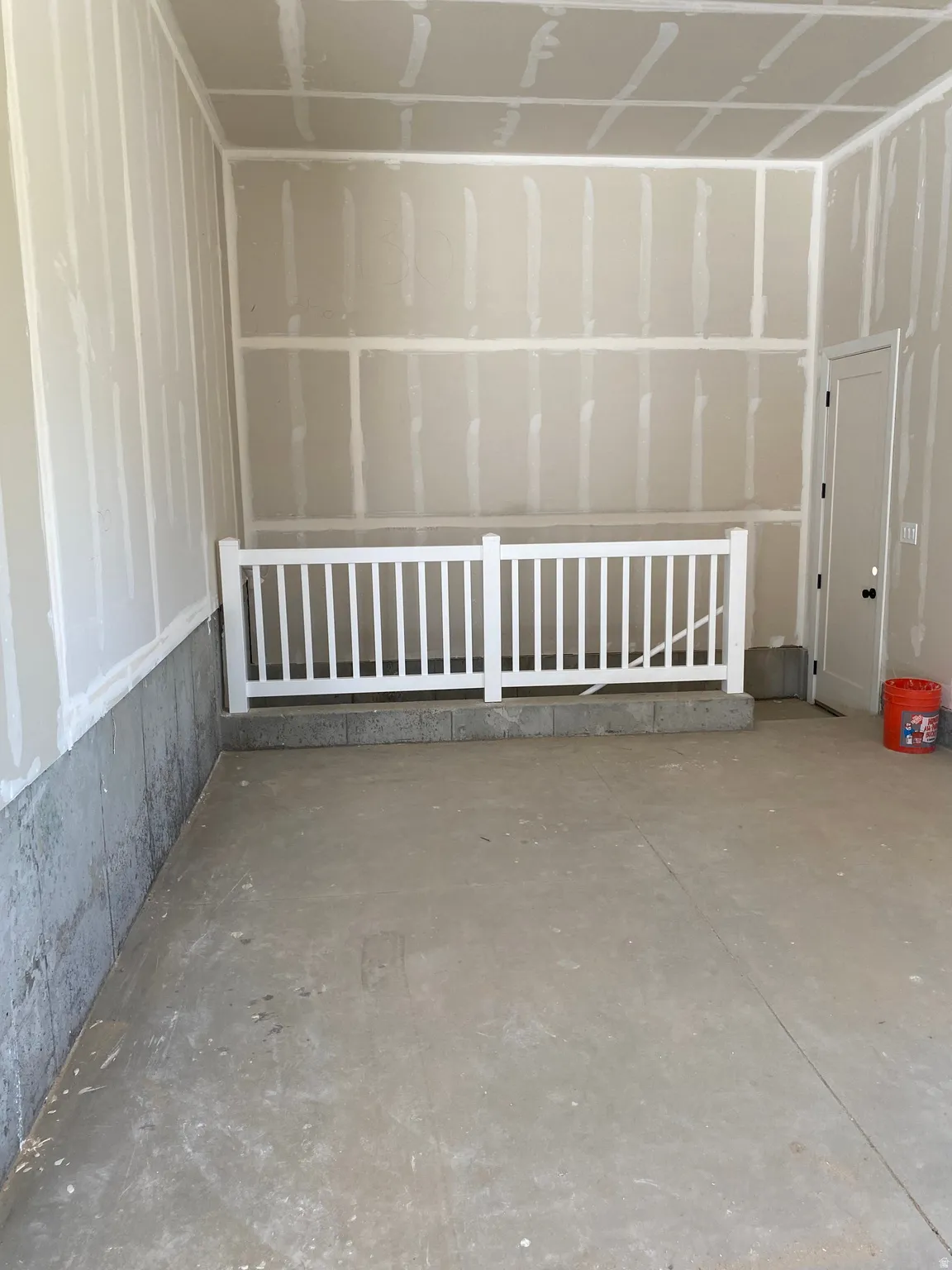 Unfinished interior space featuring a concrete floor, drywall-finished walls, and a white baluster railing