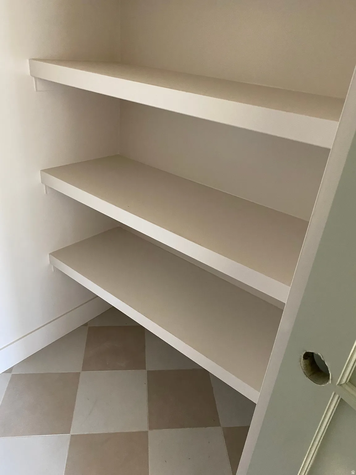Built-in shelving unit featuring three expansive shelves, white baseboards, and two-tone checkered floor tiles