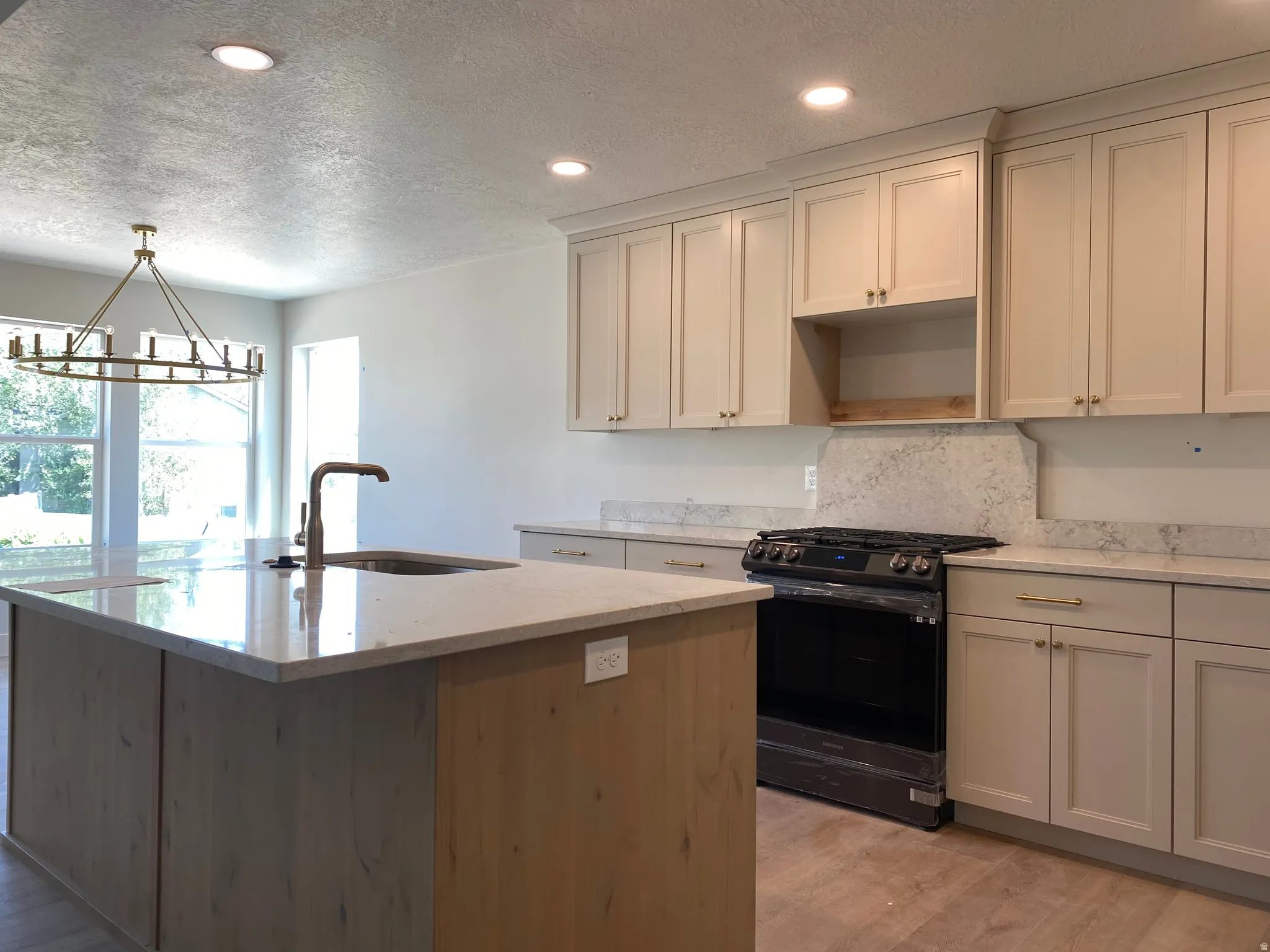 Kitchen featuring light-toned cabinetry with gold-finish hardware, a built-in range, and light-toned countertops extending to a matching backsplash