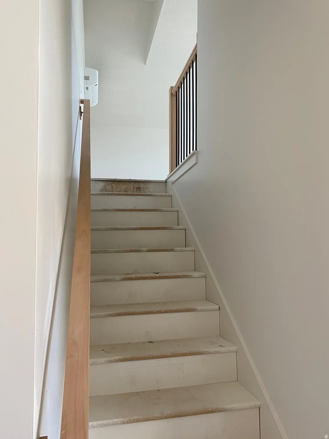 Staircase featuring a natural wood handrail, contrasting black metal balusters, and white risers