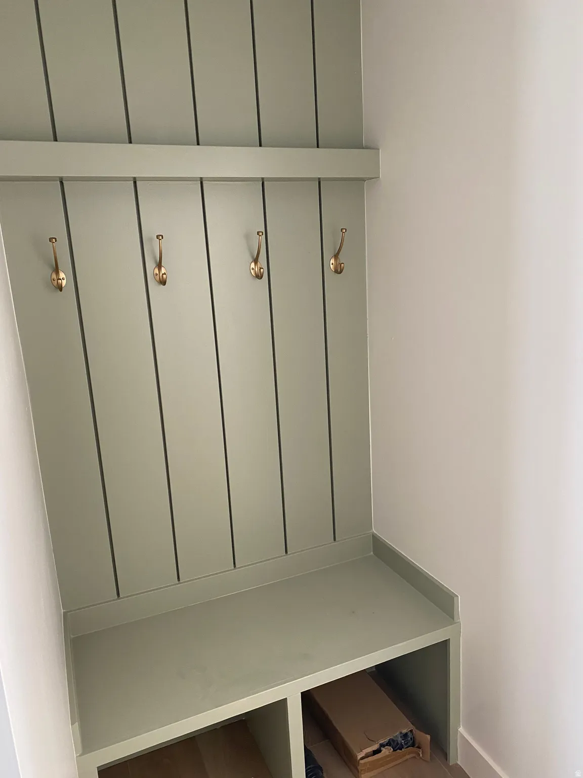 Built-in mudroom bench featuring beadboard paneling and four brass-finish hooks