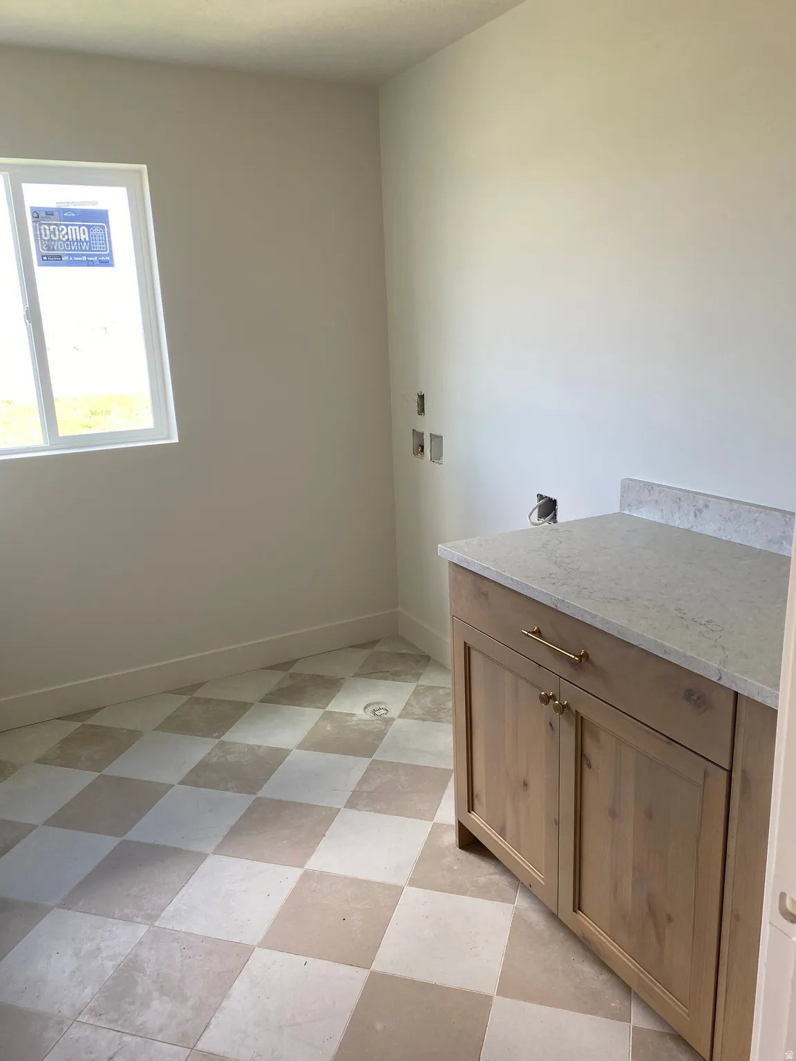 Utility room featuring a light wood-finish vanity with gold-tone hardware, a light-colored countertop, and a checkerboard-patterned floor