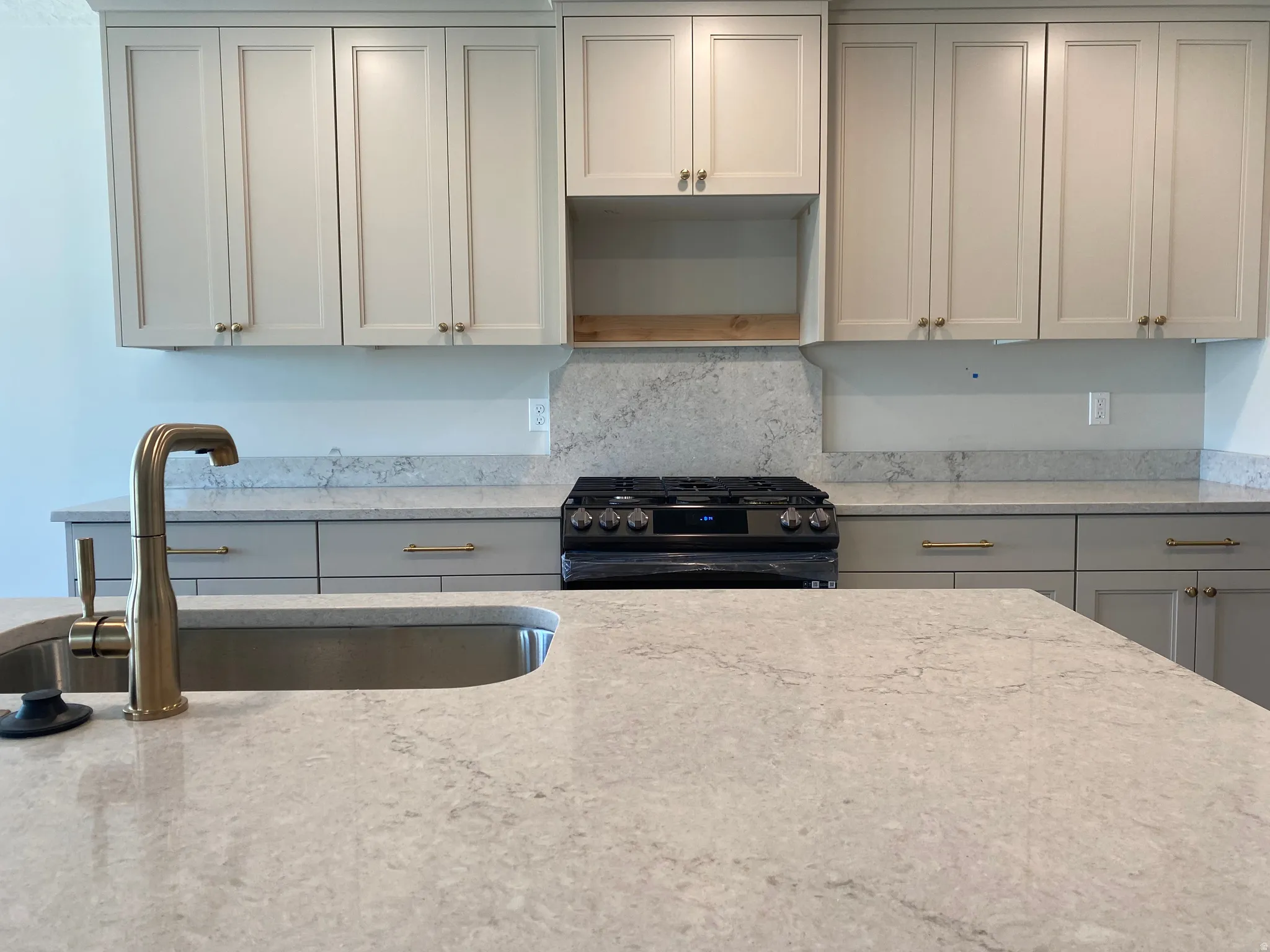 Kitchen featuring light-toned cabinetry with brass hardware, a gas range, and a coordinating stone-finish countertop and backsplash