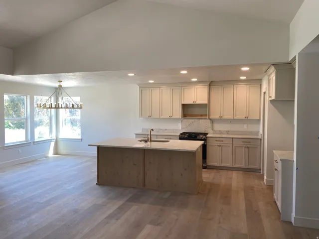 Open-concept kitchen and dining area featuring light wood-finish flooring, a vaulted ceiling, and a modern chandelier