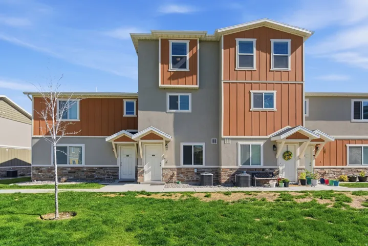 Modern multi-story exterior featuring stucco and vertical panel siding, stone veneer accents, and white-trimmed windows