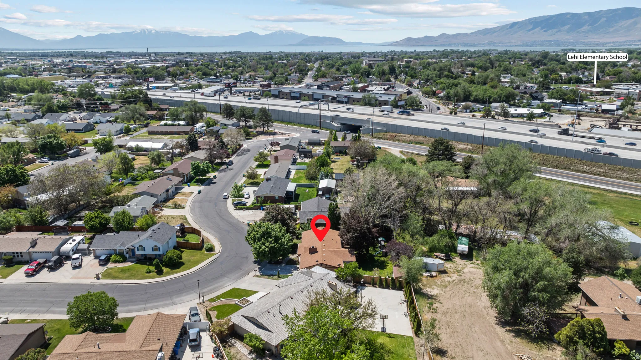 Aerial perspective showcasing a residential area with a prominent highway, surrounding green spaces, and distant mountains