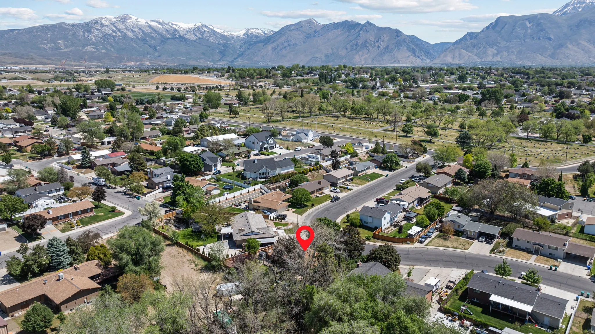 Residential neighborhood with mature trees and paved streets, framed by distant snow-capped mountains