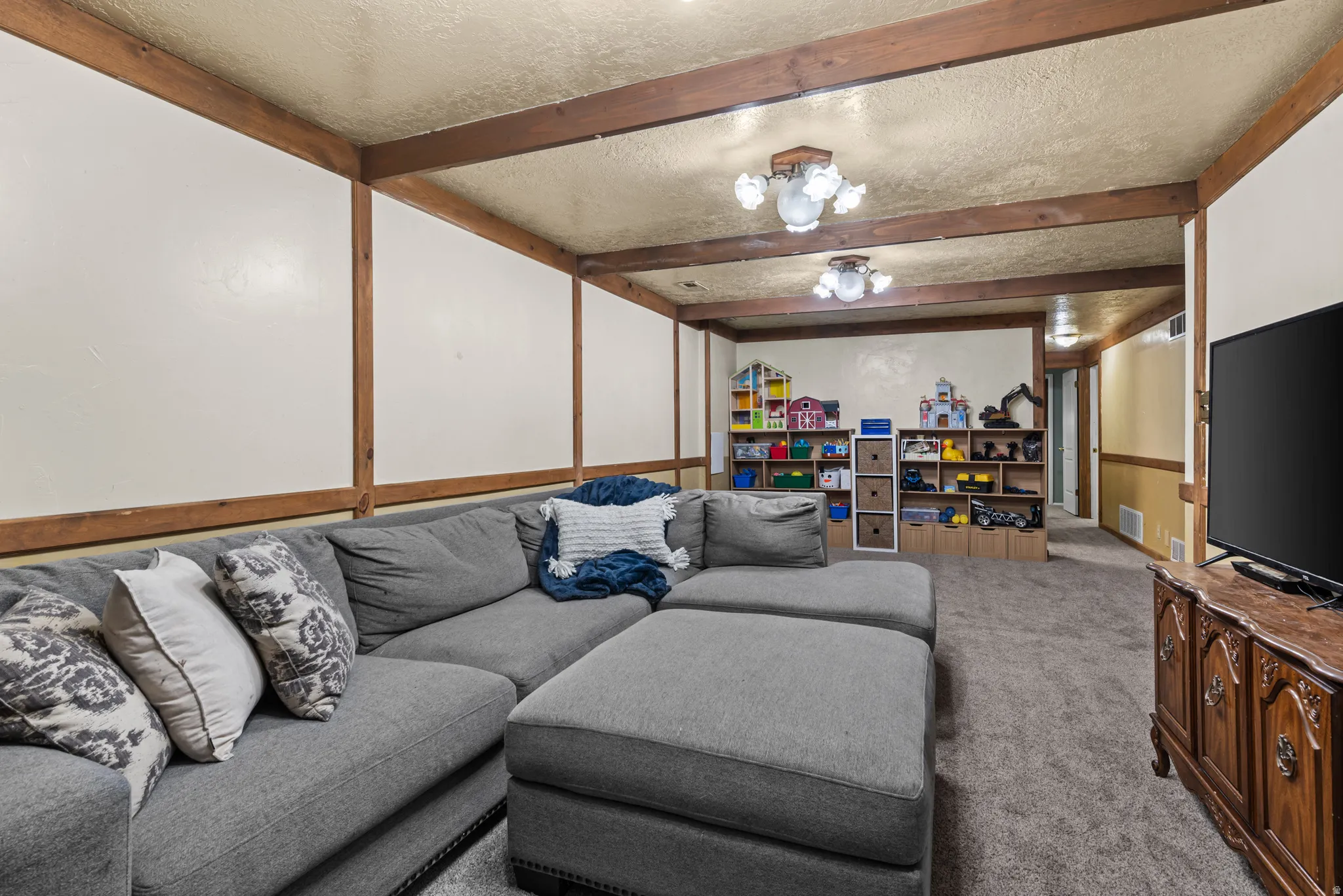 Spacious recreation room featuring exposed wood beams, a textured ceiling, recessed lighting, and soft carpet flooring
