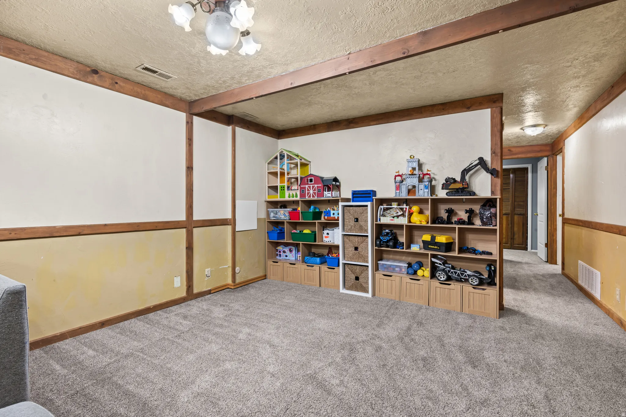 Spacious room featuring wood-finish ceiling beams, two-tone wall treatment, and gray carpet flooring