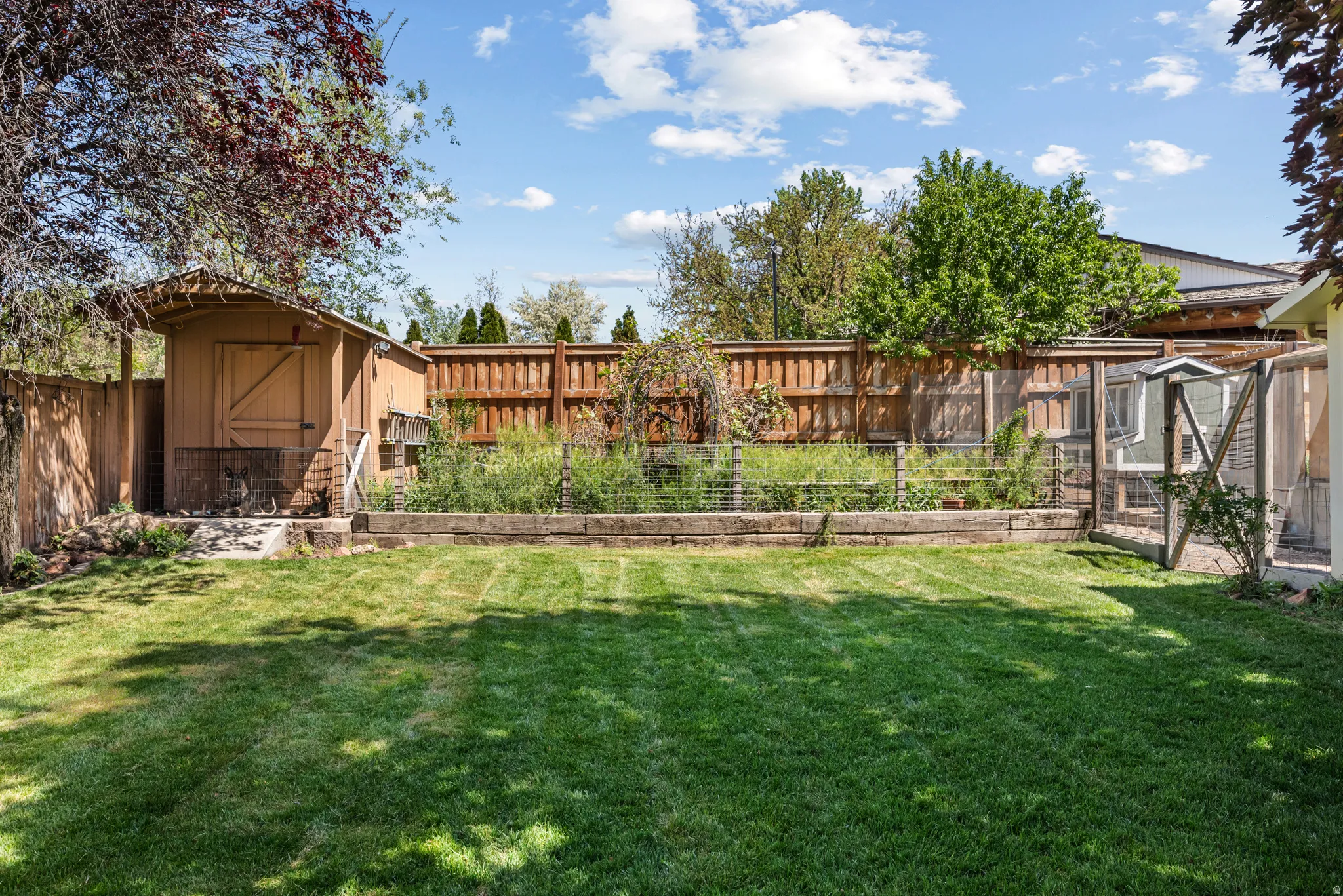 Expansive rear yard featuring a manicured lawn, a wooden storage shed, a raised garden bed with retaining timbers, and privacy fencing
