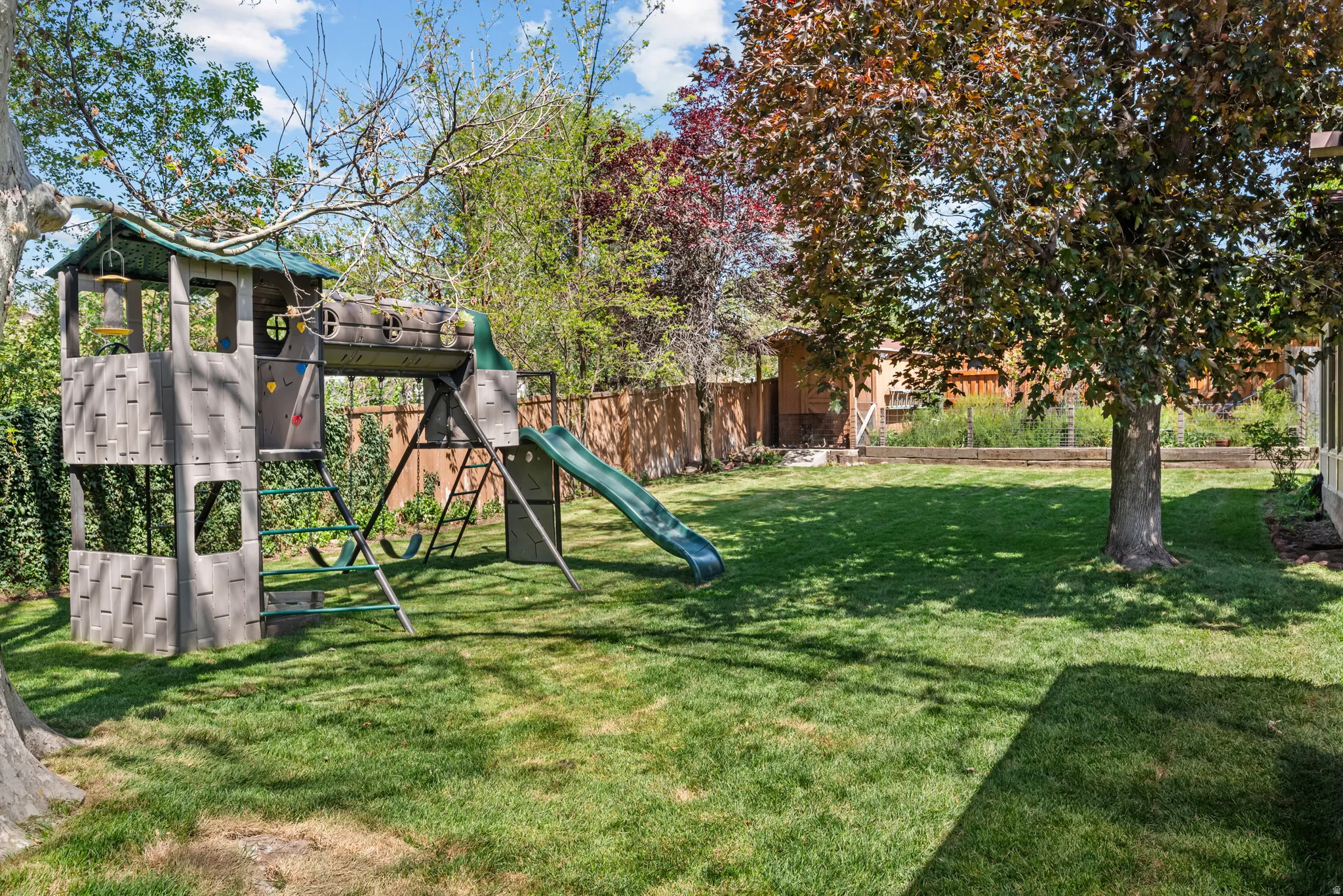 Expansive backyard featuring a lush lawn, mature trees, and a wooden privacy fence