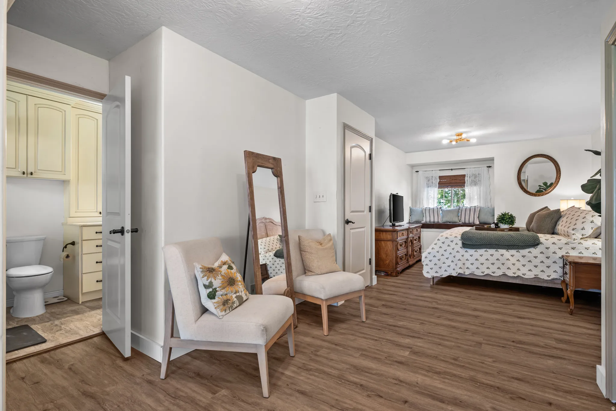 Spacious interior featuring wood-finish flooring, a built-in window bench, white walls, and a separate room with a toilet and built-in cabinetry