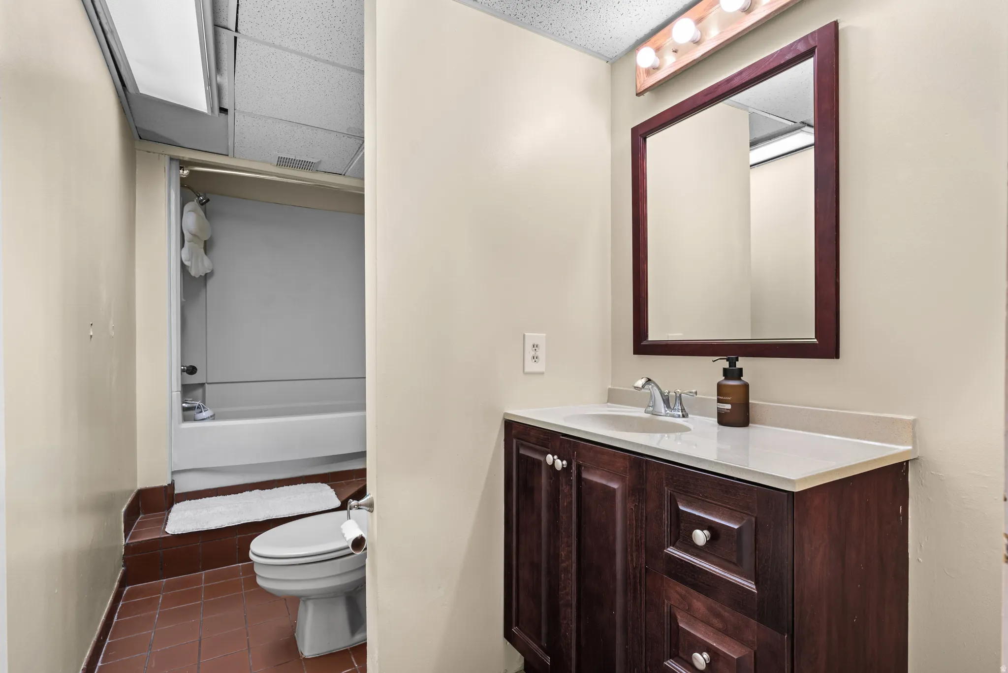 Vanity with wood-finish cabinetry, light-toned countertop, and framed mirror with overhead lighting