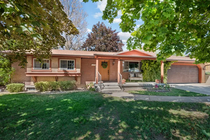 Brick ranch-style residence featuring a covered front porch, an attached two-car garage, and established front yard landscaping