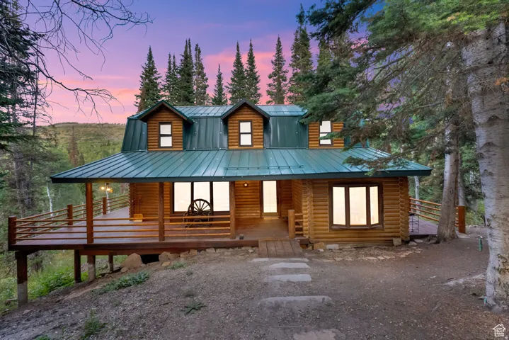 Log cabin exterior featuring a green metal roof, multiple dormer windows, and an expansive wraparound deck with wood railings