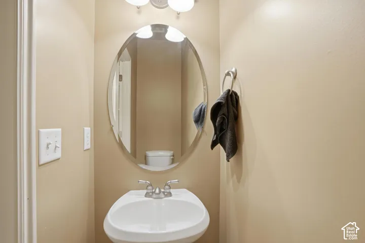 Powder bath off the back of the home, with pedestal sink with dual-handle faucet, oval mirror, and wall-mounted light fixture