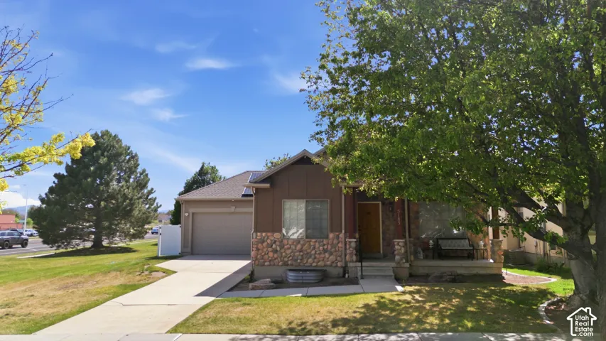 Contemporary home featuring a stone and siding exterior, an attached garage, a covered front porch, and mature trees on a corner lot