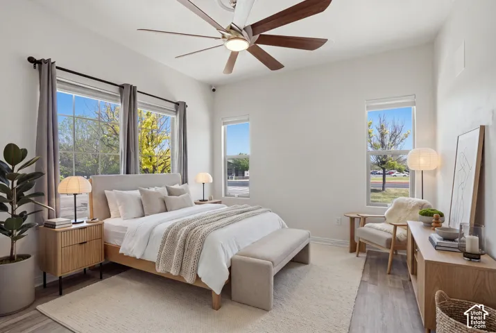 Spacious room featuring multiple windows, a ceiling fan with integrated lighting, and wood-finish flooring. (Staged)
