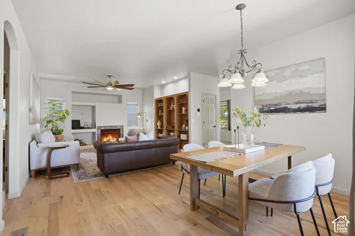 Open-concept living and dining area featuring wood-finish flooring, a fireplace with a stone surround, recessed lighting, and built-in shelving
