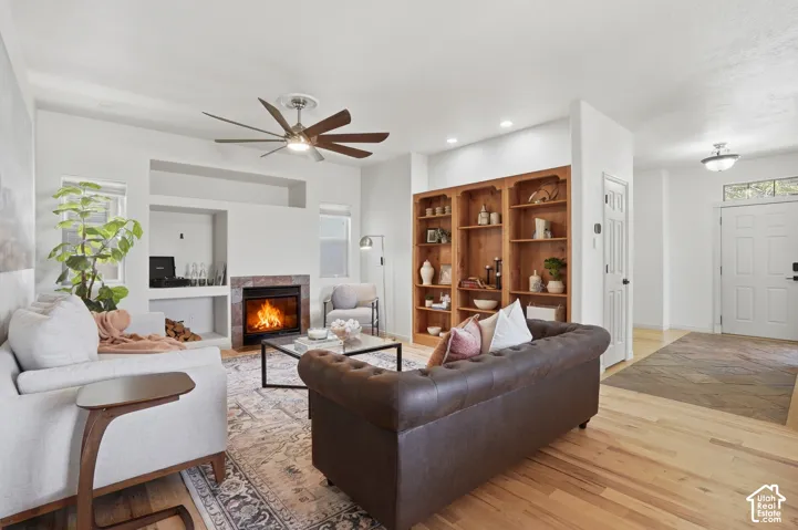 Living area featuring a fireplace with a stone surround, built-in shelving, wood-finish flooring, and a ceiling fan