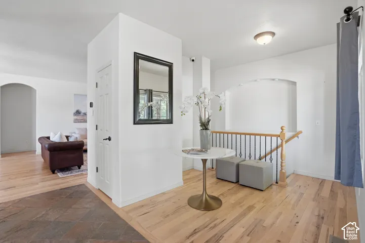 Entryway featuring wood-finish flooring, staircase with dark metal balusters, arched wall niche, and an arched doorway leading to an additional room