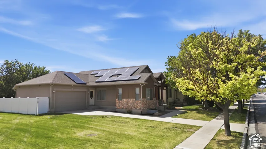 Ranch-style residence featuring solar panels, an attached two-car garage, and a partial stone facade