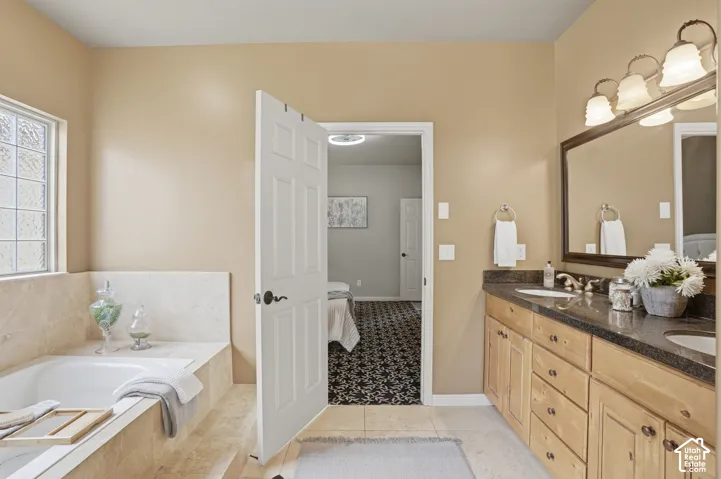 Ensuite bathroom featuring a built-in soaking tub with stone surround, a dual vanity with a dark countertop and undermount sinks, wood-finish cabinetry, and a large framed mirror. Spa like bath.