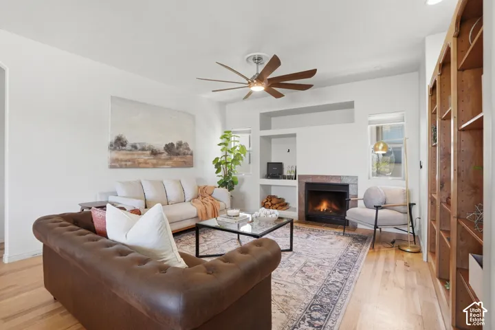 Living area featuring light wood-finish flooring, a built-in fireplace with a stone surround, recessed wall shelving, and a ceiling fan