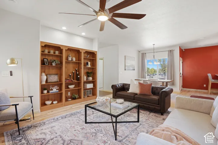 Living area featuring wood-finish flooring, built-in shelving, a ceiling fan with integrated lighting, and recessed lighting