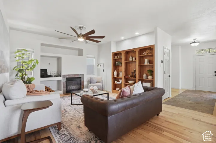 Living area featuring a ceiling fan, fireplace with stone surround, recessed shelving, and a built-in wood-finish bookcase