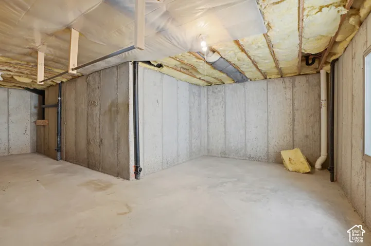 Unfinished basement space featuring concrete walls and flooring, exposed ceiling joists with insulation, and visible utility lines.  Presently storage, but could be converted to a bedroom, office, or flex space.