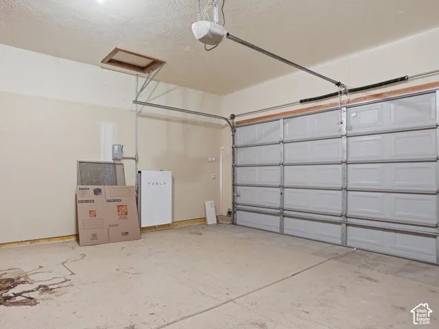 Attached two car garage featuring a sectional overhead door with an automatic opener, concrete flooring, and an attic access panel