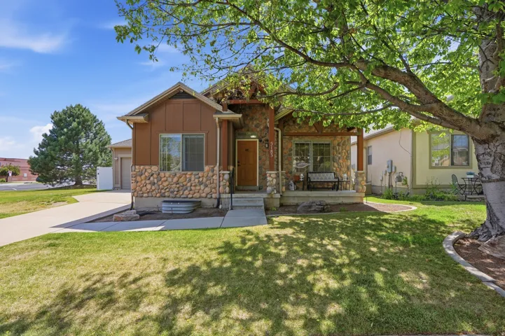 Craftsman-style exterior featuring stone and wood siding, a covered front porch, and a mature tree providing shade