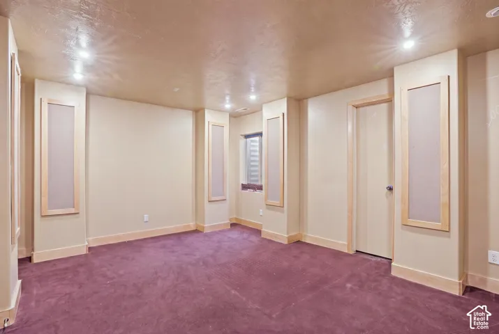 Recessed lighting illuminates a carpeted room featuring light wood trim, built-in wall panels, and a window with horizontal blinds