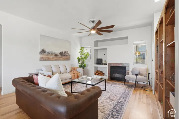 Living room featuring hardwood flooring, a ceiling fan with wood-finish blades, and a built-in fireplace with a stone surround