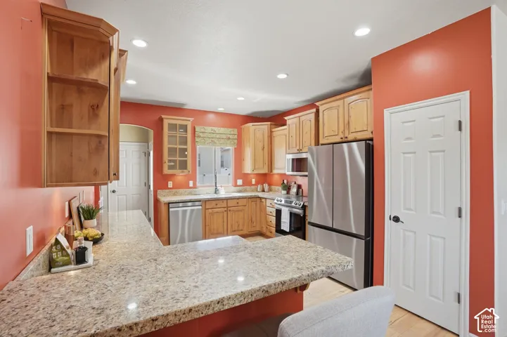 Kitchen featuring light wood cabinetry, a peninsula with a light-toned granite countertop, stainless steel appliances (included) recessed lighting, and a window with a valance