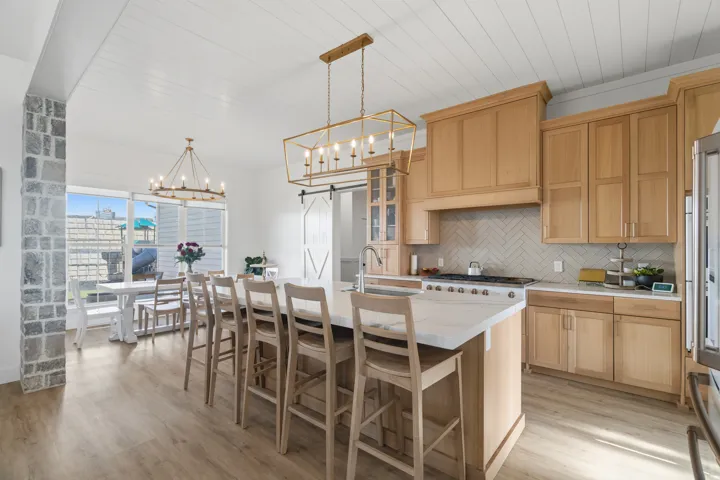 Gourmet kitchen and dining area featuring light wood cabinetry, a large center island with seating, white countertops, and a herringbone tile backsplash