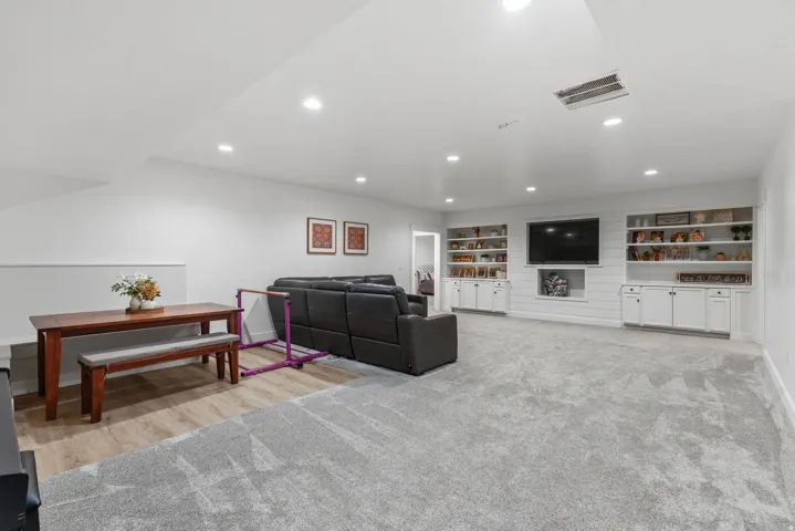 Spacious multi-zone interior featuring recessed lighting, a built-in entertainment center with open shelving and lower cabinetry, wood-finish flooring, and soft grey carpeting