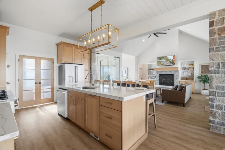 Open-concept kitchen and living area featuring a large center island with seating, natural wood cabinetry, wood-finish flooring, and a stone accent wall