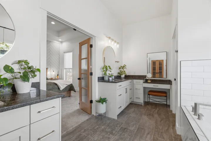 Dual vanity with dark stone countertops, white shaker cabinetry, and polished nickel hardware