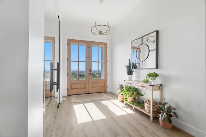 Entryway featuring light wood-finish flooring, a contemporary chandelier, double glass-paneled entry doors, and a large wall-mounted mirror