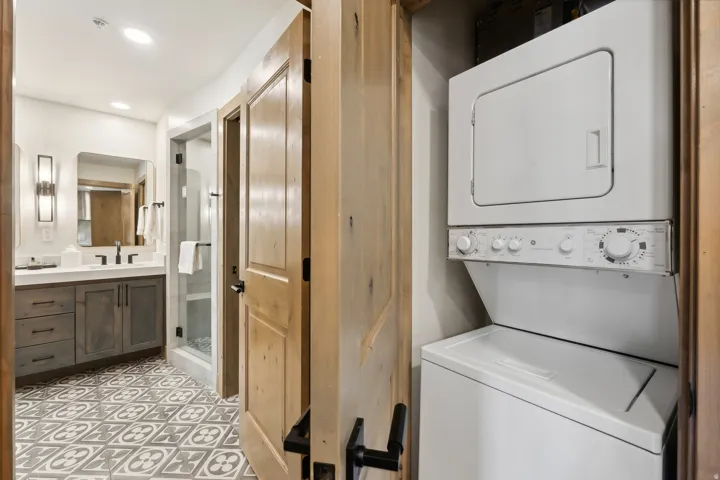 Bathroom featuring a patterned tile floor, a single vanity with a white countertop and gray cabinetry, a rectangular mirror, and wall-mounted sconces