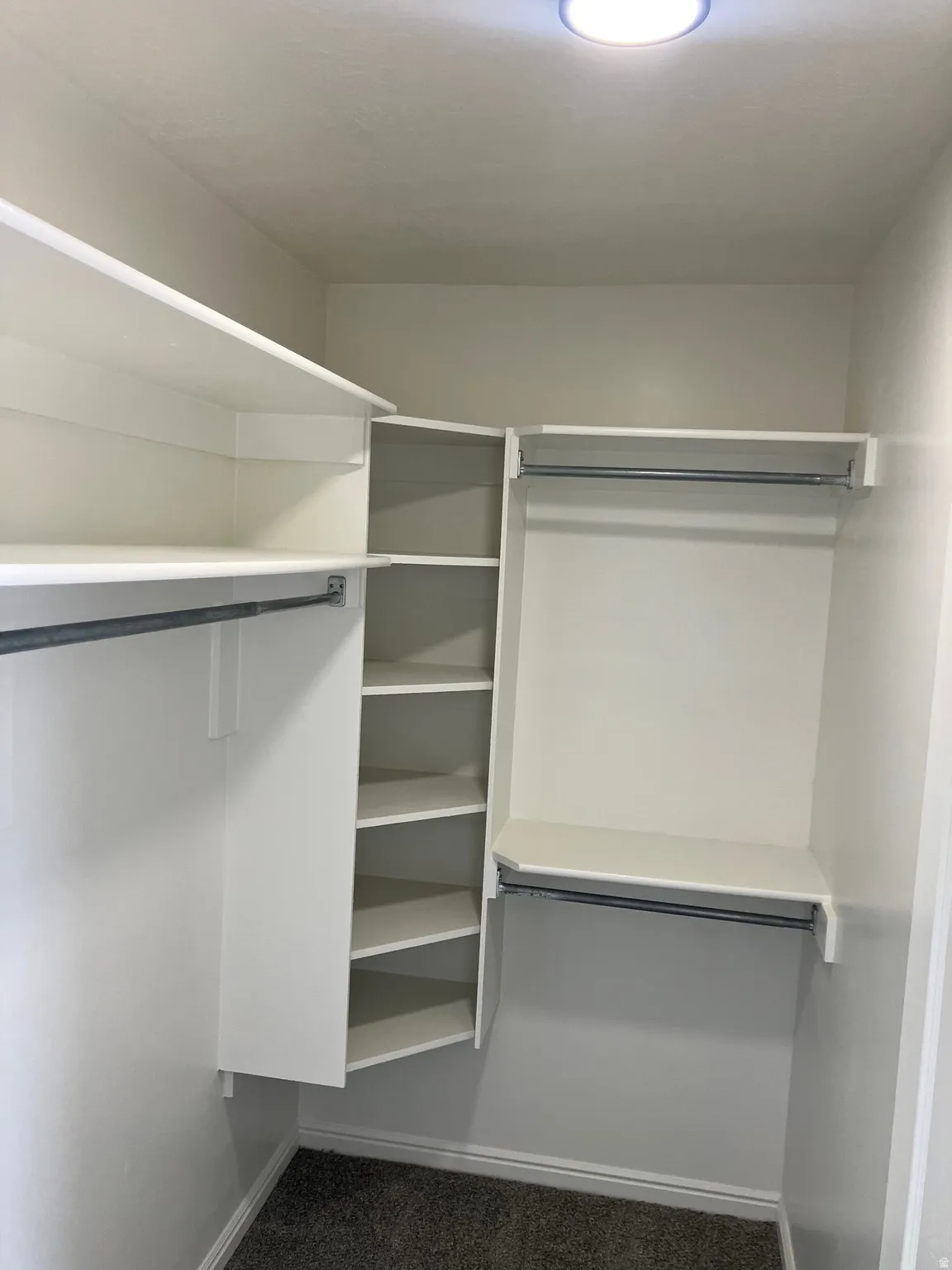 Custom closet system featuring multiple hanging rods, corner shelving, white finishes, and recessed ceiling lighting