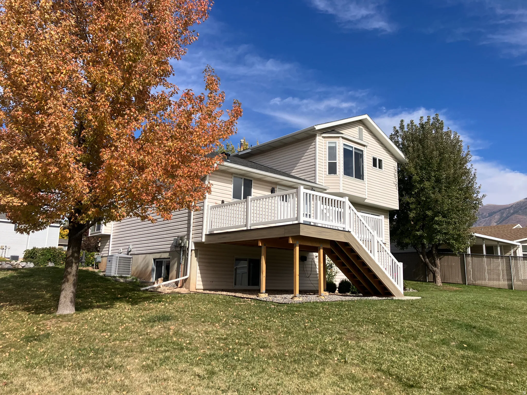 Rear exterior featuring a multi-level deck with white railings and staircase, light-toned siding, and a bay window