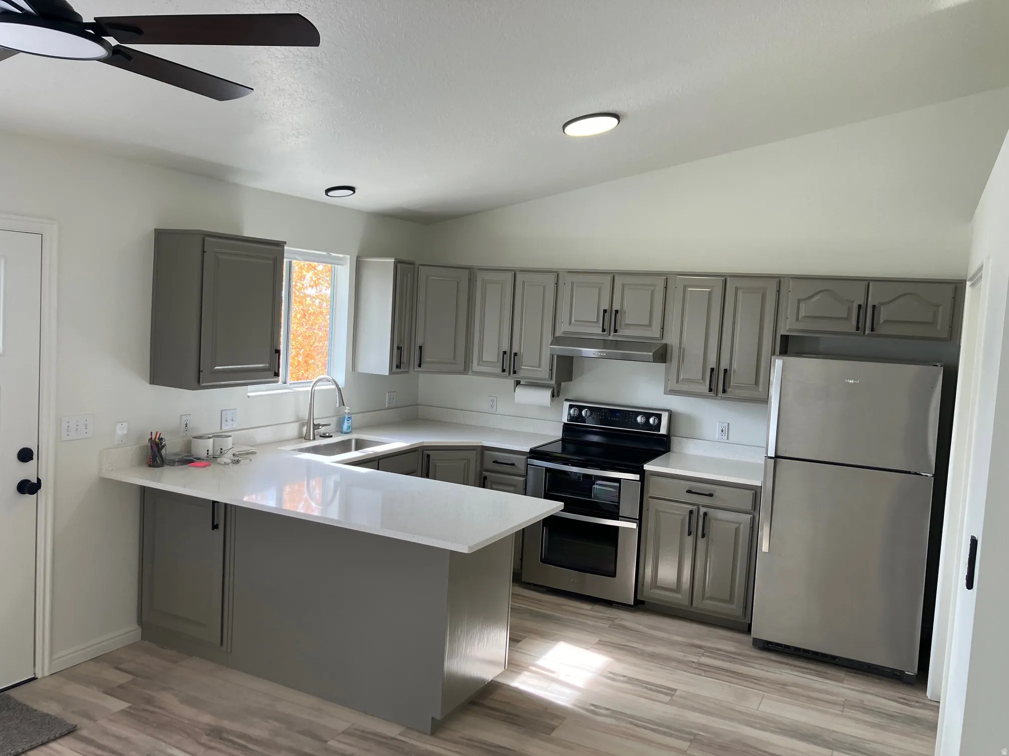Modern kitchen featuring gray cabinetry, light countertops, wood-finish flooring, stainless steel appliances, and a vaulted ceiling with recessed lighting