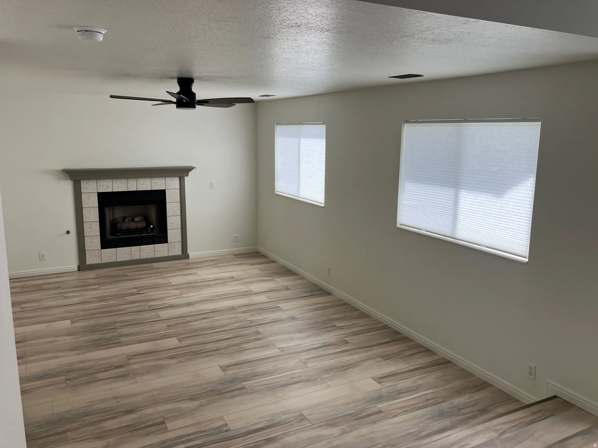 Living area featuring wood-finish flooring, a fireplace with a tiled surround and mantel, and a ceiling fan